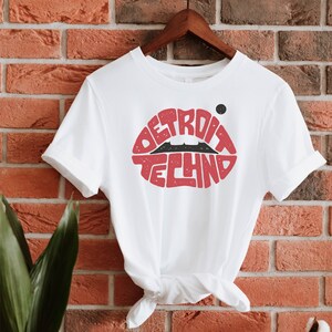 May include: White t-shirt with a red lips graphic featuring the text "DETROIT TECHNO" in black.