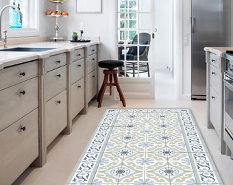 May include: A patterned kitchen rug with a geometric design in shades of blue, beige, and white. The rug is placed in a kitchen with white cabinets and a stainless steel refrigerator.