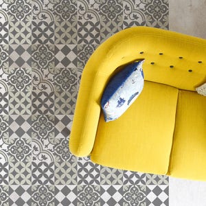 May include: A yellow couch with a blue and white patterned pillow sits on a floor with a black and white patterned tile design.