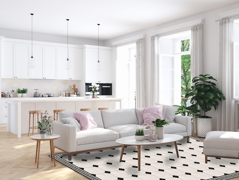 May include: A bright, modern living space with white walls, cabinetry, and furniture. A white sofa with pink pillows sits on a black and white patterned rug. The room features large windows with white curtains, and a kitchen island with bar stools.