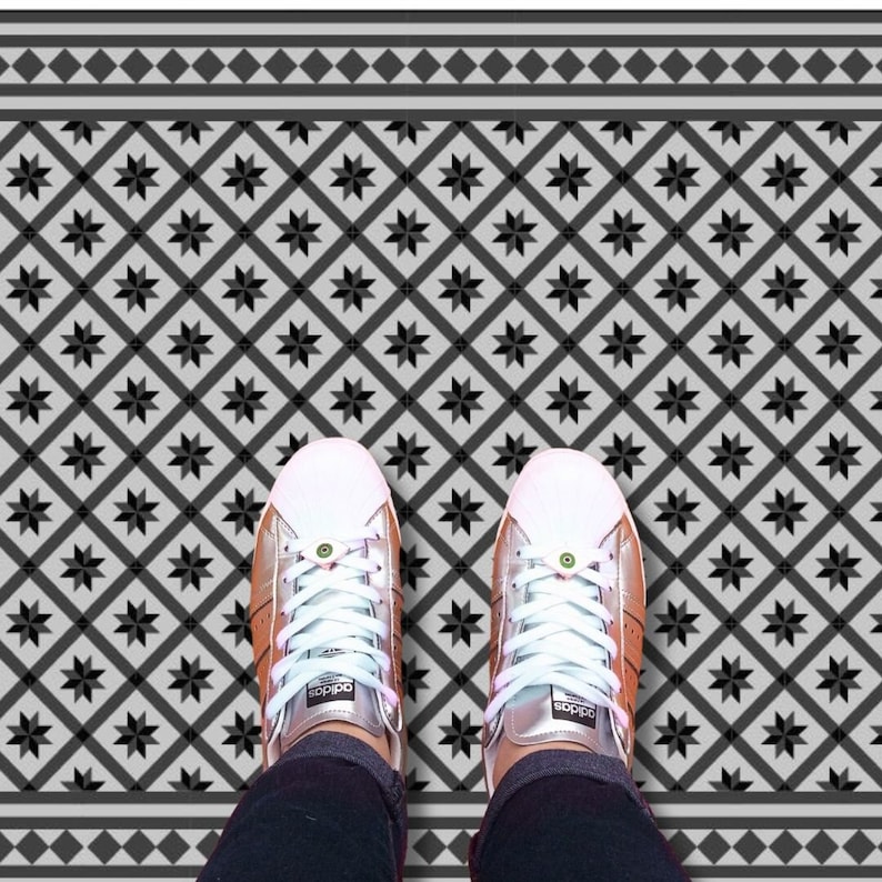 May include: A pair of white sneakers with black accents on a black and white patterned floor. The floor has a geometric design with black stars and white diamonds.