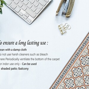 May include: A patterned rug with a blue, orange, and white design. The rug has a border with a repeating pattern. The text on the image reads: "To ensure a long lasting use: * Clean with a damp cloth * Do not use harsh cleaners such as bleach * There Periodically ventilate the bottom of the carpet * For indoor use only - Can be used in shaded patio /balcony"