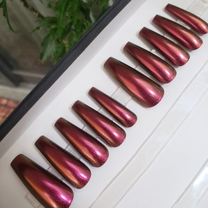 Puede incluir: Un juego de diez uñas postizas largas en forma de ataúd con un acabado iridiscente burdeos oscuro.