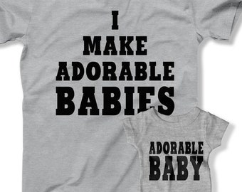 Könnte beinhalten: Ein graues T-Shirt und ein Baby-Body-Set. Das Erwachsenen-Shirt trägt den Aufdruck "I MAKE ADORABLE BABIES" in fetten schwarzen Buchstaben. Der Baby-Body trägt in der gleichen Schriftart "ADORABLE BABY". Beide Artikel sind aus weichem Material.