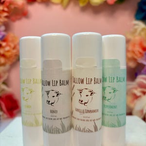 May include: Four white tubes of lip balm with different flavors: Lemon, Honey, Vanilla Cinnamon, and Peppermint. Each tube has a brown cow illustration and the text "Tallow Lip Balm".