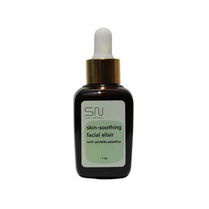 May include: A dark brown glass bottle with a gold cap and white dropper. The label reads "skin-soothing facial elixir" with "centella asiatica" and "1 oz". The bottle has a square shape with rounded edges.