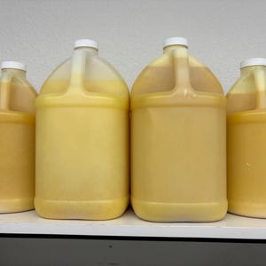 May include: Five clear plastic gallon jugs filled with a yellow liquid. The jugs have white lids.