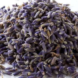 May include: A close-up of a pile of dried lavender buds. The buds are a deep purple color and have a slightly fuzzy texture.