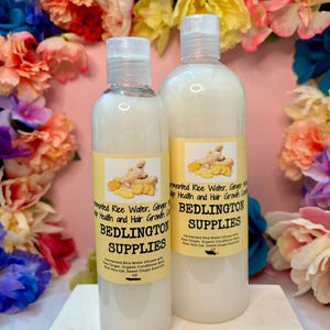May include: Two clear plastic bottles filled with a white liquid, each featuring a yellow label with an image of ginger root. The labels display the text Bedlington Supplies, Fermented Rice Water, Ginger, and Hair Growth Conditioner.