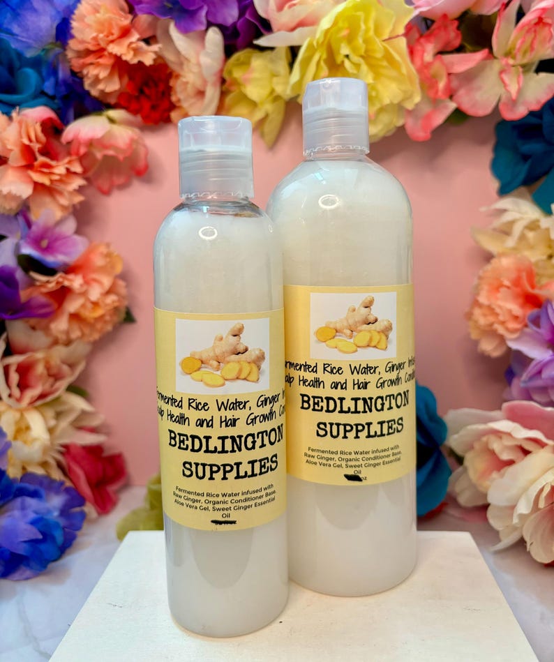 May include: Two clear plastic bottles filled with a white liquid, each featuring a yellow label with an image of ginger root. The labels display the text Bedlington Supplies, Fermented Rice Water, Ginger, and Hair Growth Conditioner.