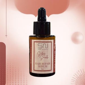 K&ouml;nnte beinhalten: Eine braune Glasflasche mit Haar-Reparatur-Serum und einer schwarzen Pipette. Auf dem Etikett steht "SN SEOUL NATURALS Silky Smooth HAIR REPAIR SERUM 1oz". Der Hintergrund ist ein Farbverlauf aus Rosa und Pfirsich.