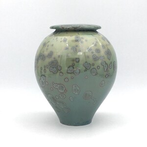 May include: A ceramic urn with a light green and white glaze. The glaze has a speckled pattern with small, dark blue spots.