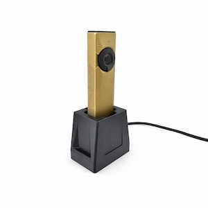 May include: A gold-colored electronic device with a black circular button and a black base. The device is rectangular and has text on its side. A black cable extends from the base.