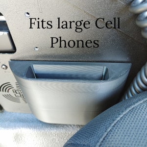 Puede incluir: Un soporte para tel&eacute;fono de pl&aacute;stico negro que se adapta a tel&eacute;fonos grandes. El soporte est&aacute; montado en un coche y dice "Fits large Cell Phones".