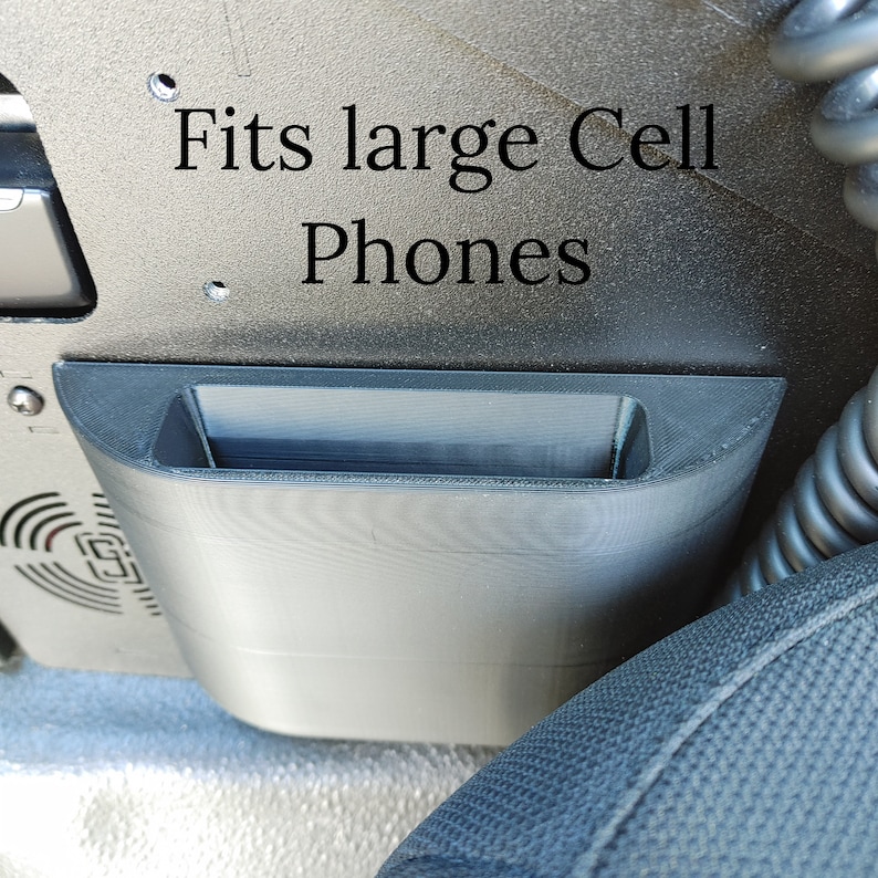 Puede incluir: Un soporte para tel&eacute;fono de pl&aacute;stico negro que se adapta a tel&eacute;fonos grandes. El soporte est&aacute; montado en un coche y dice "Fits large Cell Phones".