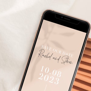 Puede incluir: La pantalla de un tel&eacute;fono inteligente muestra un anuncio de guardar la fecha para la boda de Rachel y Steven el 10.08.2023. El fondo es de color melocot&oacute;n claro con una sombra de hojas.