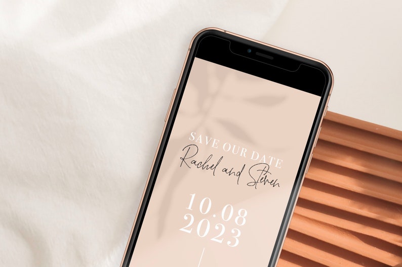 Puede incluir: La pantalla de un tel&eacute;fono inteligente muestra un anuncio de guardar la fecha para la boda de Rachel y Steven el 10.08.2023. El fondo es de color melocot&oacute;n claro con una sombra de hojas.