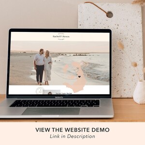 May include: A laptop computer displaying a wedding website with a photo of a couple on a beach. The website features the couple's names, "Rachel & Steven", and a map with a heart marking their wedding location. The text "VIEW THE WEBSITE DEMO" is displayed below the laptop.