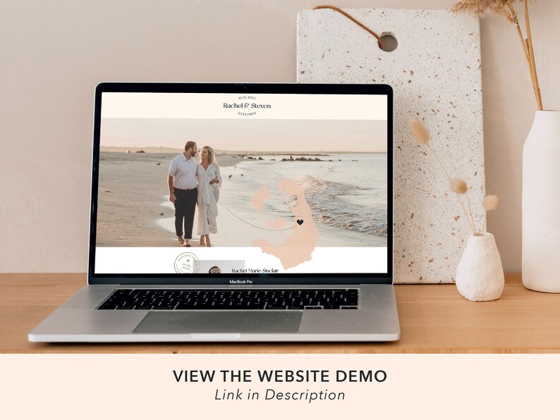 May include: A laptop computer displaying a wedding website with a photo of a couple on a beach. The website features the couple's names, "Rachel & Steven", and a map with a heart marking their wedding location. The text "VIEW THE WEBSITE DEMO" is displayed below the laptop.