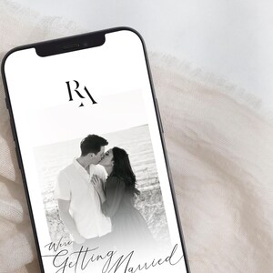 May include: A black and white photo of a couple kissing on a beach. The photo is on a smartphone screen with the text "We're Getting Married" and the initials "RA" at the top.