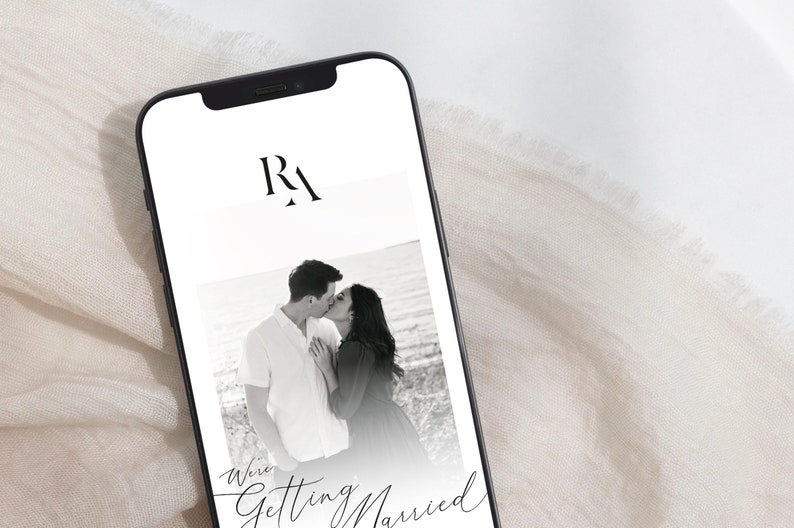 May include: A black and white photo of a couple kissing on a beach. The photo is on a smartphone screen with the text "We're Getting Married" and the initials "RA" at the top.