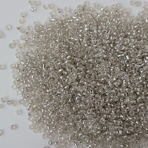 Könnte beinhalten: Ein großer Haufen kleiner, transparenter Glasperlen. Die Perlen sind auf einer weißen Oberfläche verstreut.