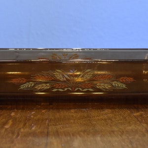 Könnte beinhalten: Eine braune Glasbackform mit einem Weizenmuster. Die Form hat zwei Griffe an den Seiten.