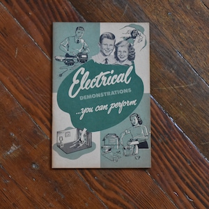 Könnte beinhalten: Eine Vintage-Broschüre mit dem Titel "Electrical Demonstrations...you can perform" mit Illustrationen von Personen und Elektrogeräten. Das Cover ist türkis und weiß, mit einem Retro-Design. Die Broschüre liegt auf einer Holzoberfläche.