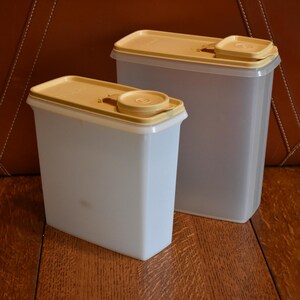 May include: Two clear plastic containers with yellow lids. The containers are rectangular and have a spout for dispensing. The containers are on a wooden surface.