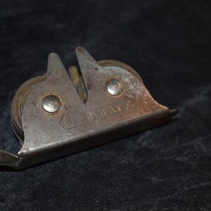 Puede incluir: Afilador de cuchillos de metal vintage con mango de madera. El afilador tiene un cuerpo plateado con dos gu&iacute;as de afilado anguladas y un rodillo. La palabra "KW" est&aacute; estampada en el metal.