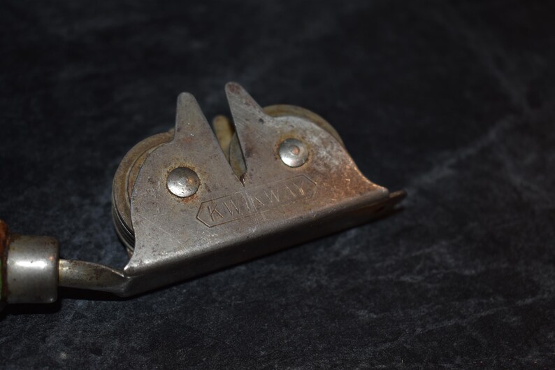 Puede incluir: Afilador de cuchillos de metal vintage con mango de madera. El afilador tiene un cuerpo plateado con dos gu&iacute;as de afilado anguladas y un rodillo. La palabra "KW" est&aacute; estampada en el metal.