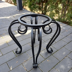 May include: Black metal table base with a round top and ornate legs. The base is made of wrought iron and has a black finish.