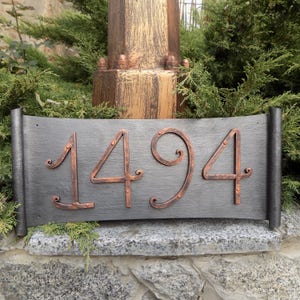 May include: A black metal house number sign with copper numerals, the number 1494 is displayed on the sign.