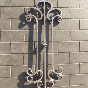 May include: A silver metal decorative wall accent with a stylized design resembling a tree with branches. The accent is mounted on a gray brick wall.