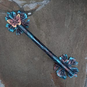 May include: A decorative wand with a butterfly and floral design. The wand is dark blue with a textured finish. The butterfly is copper-colored, and the flowers are blue and pink.