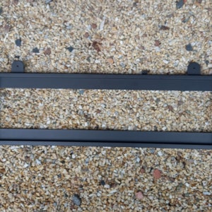 Può includere: Telaio in metallo nero con due barre orizzontali. Il telaio è progettato per contenere oggetti come foto o opere d'arte. Ha due piccoli ganci in metallo nella parte superiore per appenderlo.