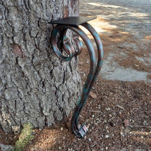 May include: A decorative metal table leg with a scrolled design. The leg is painted in a blue and copper patina finish. The leg has a small square shelf on top.