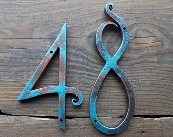 Puede incluir: Un letrero de número de casa de metal turquesa y cobre con los números 48. Los números son estilizados y tienen un aspecto rústico.