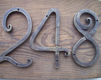 May include: A set of three metal house numbers, 248, with a rustic, hand-forged style. The numbers are attached to a wooden surface.