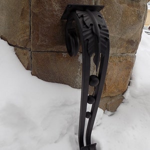 May include: Black metal scrollwork with a leaf design and three round accents. The scrollwork is attached to a stone wall and is partially covered in snow.