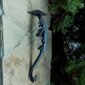 May include: Black metal handrail with a decorative leaf design. The handrail is mounted to a stone wall.