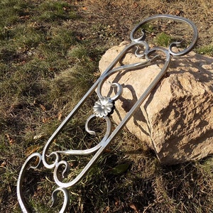 May include: A silver metal decorative piece with a floral design. The piece is made of twisted metal and has a circular top and bottom.