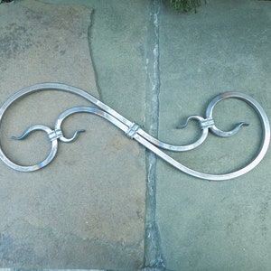 Puede incluir: Una pieza de metal decorativa con un diseño de doble bucle, que se asemeja a un símbolo de infinito. La pieza está hecha de metal plateado y tiene un acabado liso y pulido.