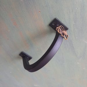 May include: Black metal handle with a decorative bee design. The handle is mounted to a wall.