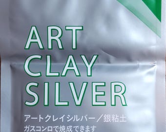 May include: A silver and green foil packet of Art Clay Silver, featuring the text "ART CLAY SILVER" in large green letters. The packaging includes Japanese text, a green circular badge indicating 7g, and the "ART CLAY Eco Friendly" logo.