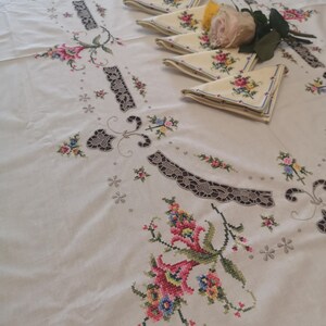 Puede incluir: Mantel blanco con delicado bordado floral en tonos rosa, amarillo y verde. El mantel presenta un dise&ntilde;o central con un borde festoneado y encaje intrincado.