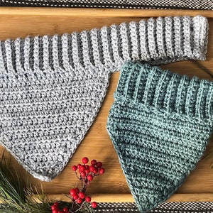 May include: Two crocheted triangle scarves, one gray and one teal green, on a wooden tray with pine sprigs and red berries.
