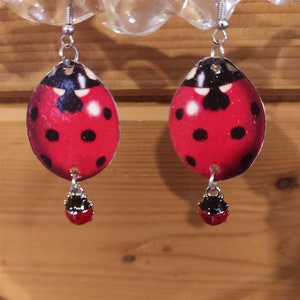 May include: A pair of red ladybug earrings with black spots and silver hooks. Each earring features a smaller ladybug charm dangling below the larger ladybug.