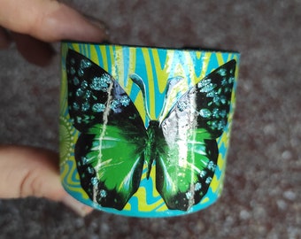 Cardboard cuff bracelet of a butterfly with glitter on a vintage green and blue paper background in cut-out paper collage "BUTTERFLY"