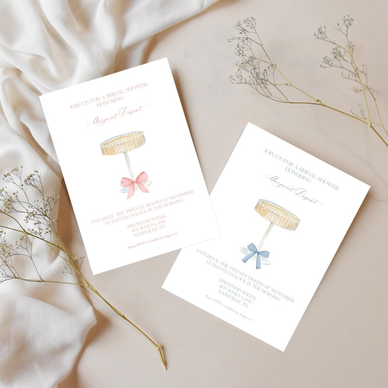 K&ouml;nnte beinhalten: Zwei wei&szlig;e Einladungskarten mit einer Aquarell-Illustration eines Kuchengestells mit einer rosa und blauen Schleife. Der Text auf den Karten lautet "Schlie&szlig;en Sie sich uns zu einer Bridal Shower zu Ehren von Margaret Dapurt an".